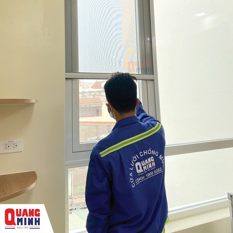 một người đàn ông mặc áo kỹ thuật đang mở cửa lưới chống muỗi tự cuốn dọc được lắp tại vị trí cửa sổ.