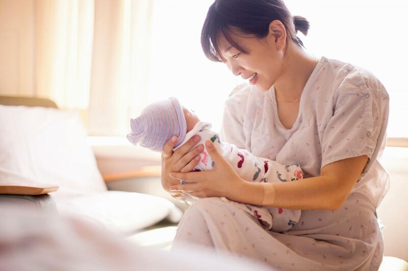 Một người phụ nữ vừa ngồi trên ghế vừa bế một em bé sơ sinh