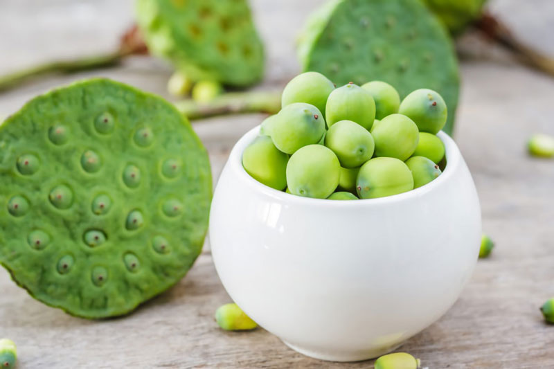 Hạt sen nguyên vỏ được đặt trong một chén trắng, bên ngoài là các cành nhụy sen