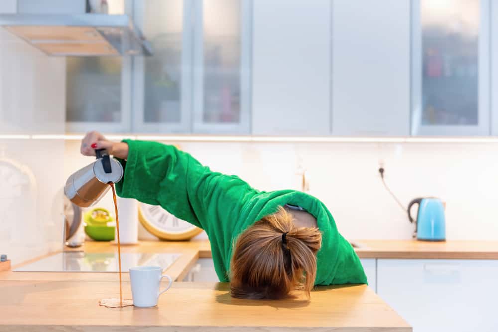 Một cô gái đang nằm gục xuống bàn, tay đang rót cà phê đổ ra ngoài