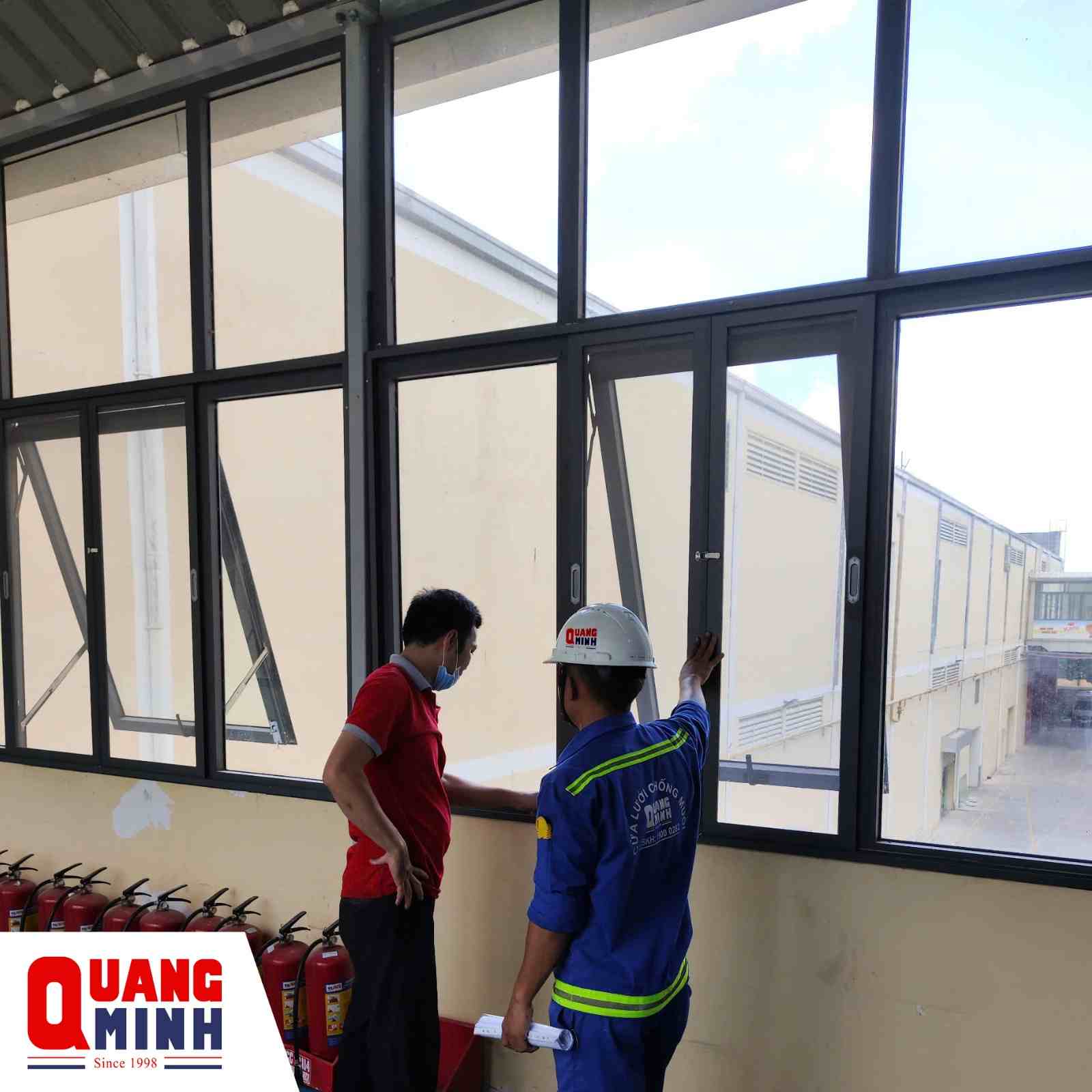 Kỹ thuật Quang Minh và khách hàng đang đứng nói chuyện gần cửa số có lắp cửa lưới chống muỗi